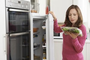 Woman grabbing bagged lettuce from the refrigerator and examining it.