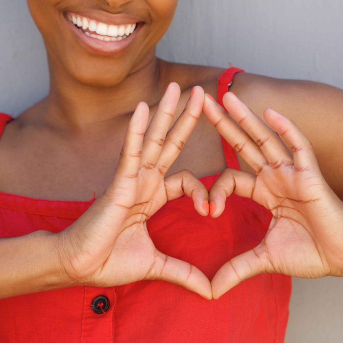 Woman in red dress making heart symbol with her hands.