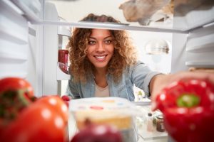 Woman reaching into fridge to grab bell pepper