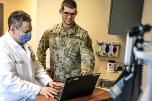 man in military uniform standing with physician looking at laptop computer