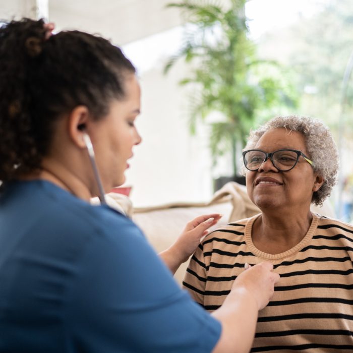 Nurse listening to senior patient's heartbeat during home visit