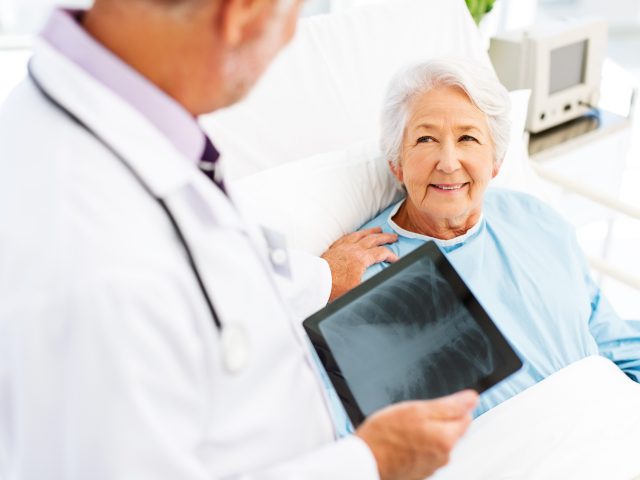 Woman Looking At Doctor With X-Ray On Digital Tablet