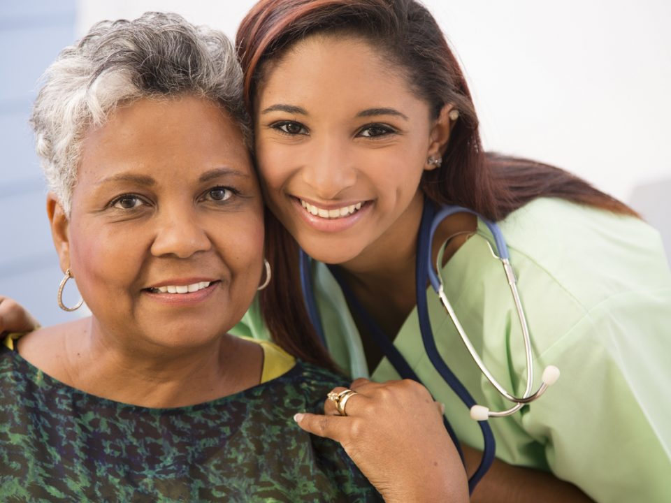 Caring, mixed-race nurse or care giver gives a senior adult, African descent patient a reassuring hug in hospital or clinic setting. Headshot.