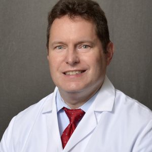Photo of Doctor Justin Szawlewicz pictured in a white lab coat and red tie