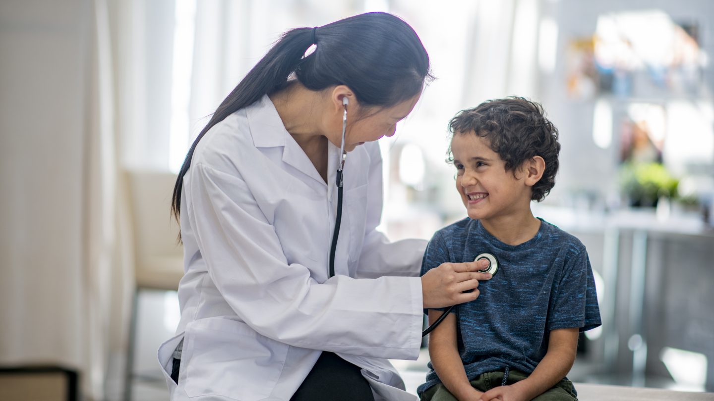 Boy smiling while the doctor checks his heart rate with a stethoscope.