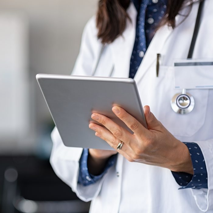 Closeup of female doctor in labcoat and stethoscope holding digital tablet, reading patient report.