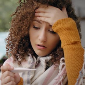 Woman holding her head and thermometer.