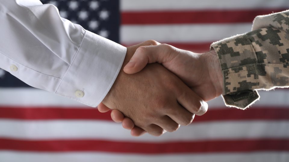 Soldier and businessman shaking hands against flag of USA, closeup