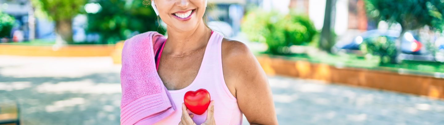 Middle age sportswoman asking for health care holding heart at the park